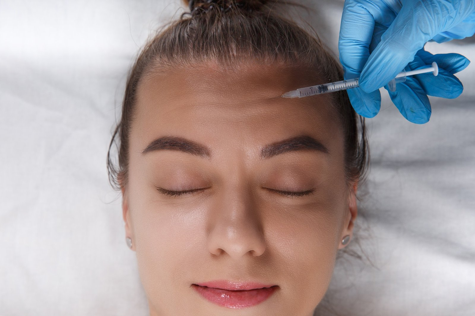 Portrait of young Caucasian woman getting cosmetic injection of botox in forehead. People